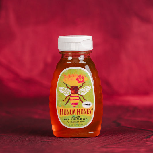 Honua Honey jar with a bee design on a red fabric background. Organic Honua Wilelaiki Honey
